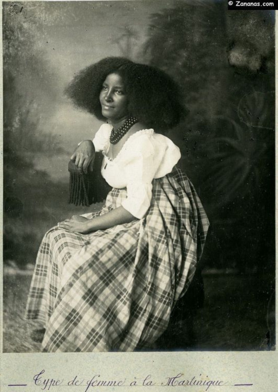 Carte postale ancienne : une femme assise en robe à carreaux.